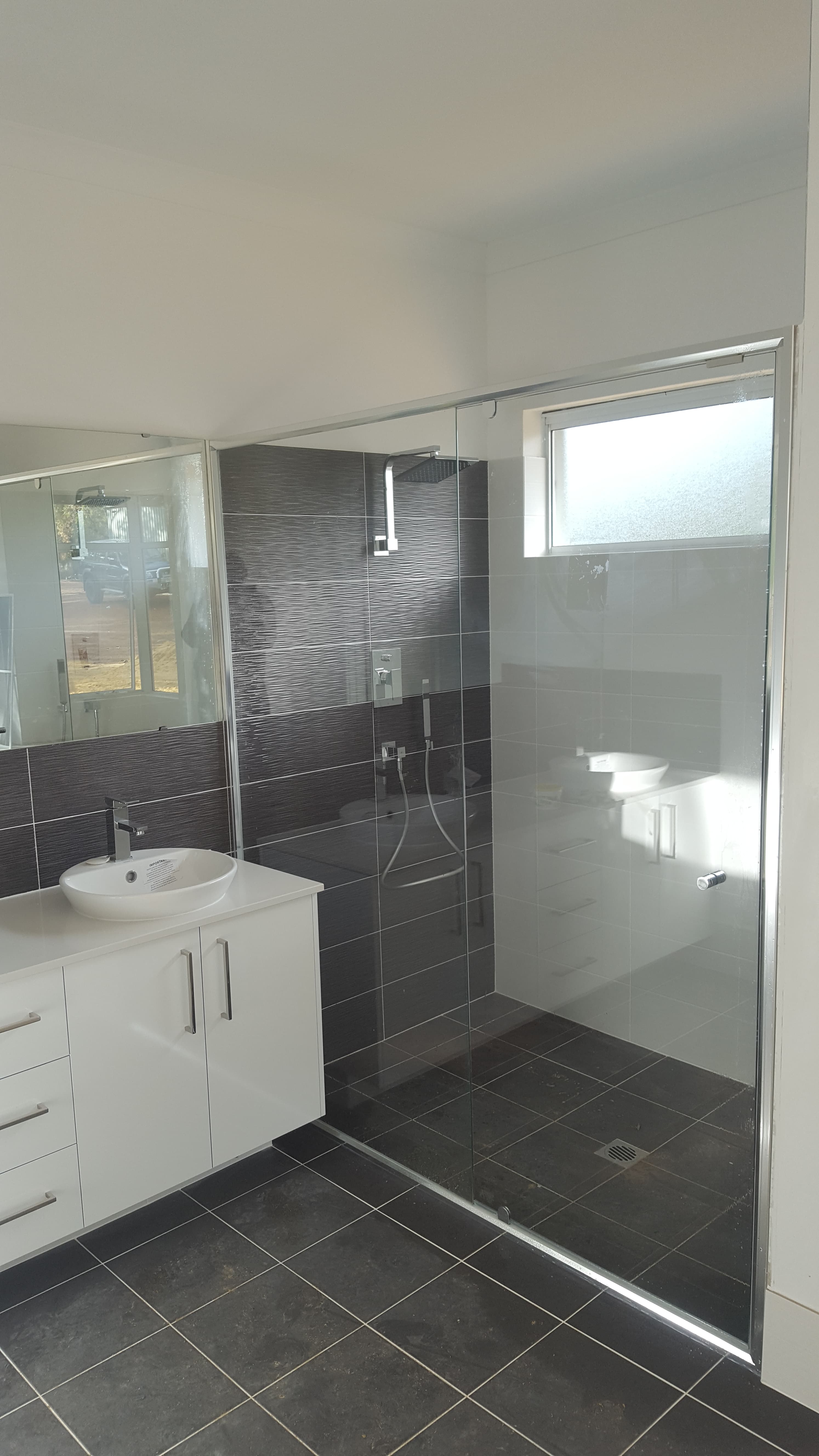 Modern bathroom with a white vanity, vessel sink, and glass-enclosed shower with dark textured tiling.