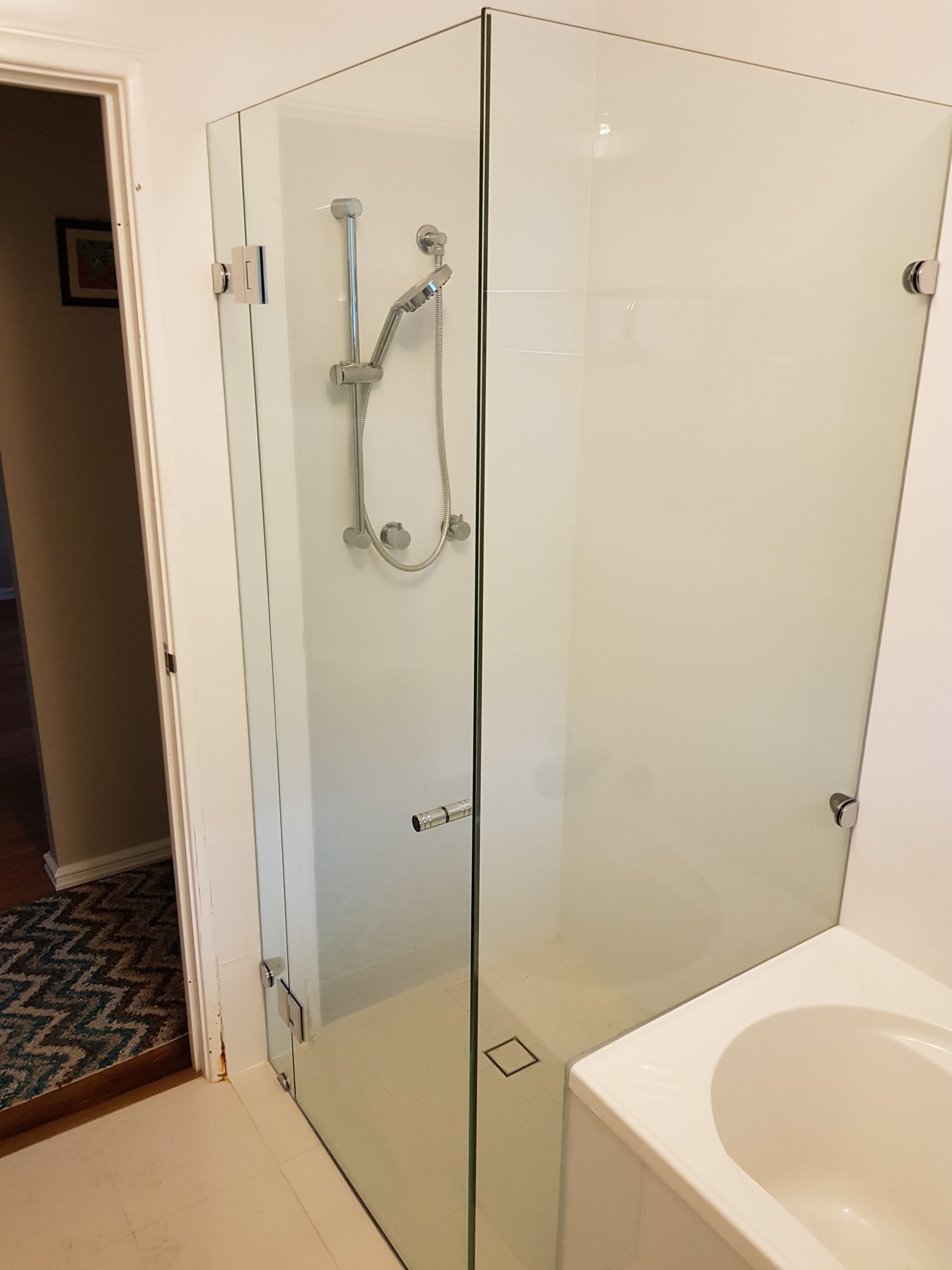 Frameless glass shower with chrome fixtures and a handheld showerhead next to a white bathtub.