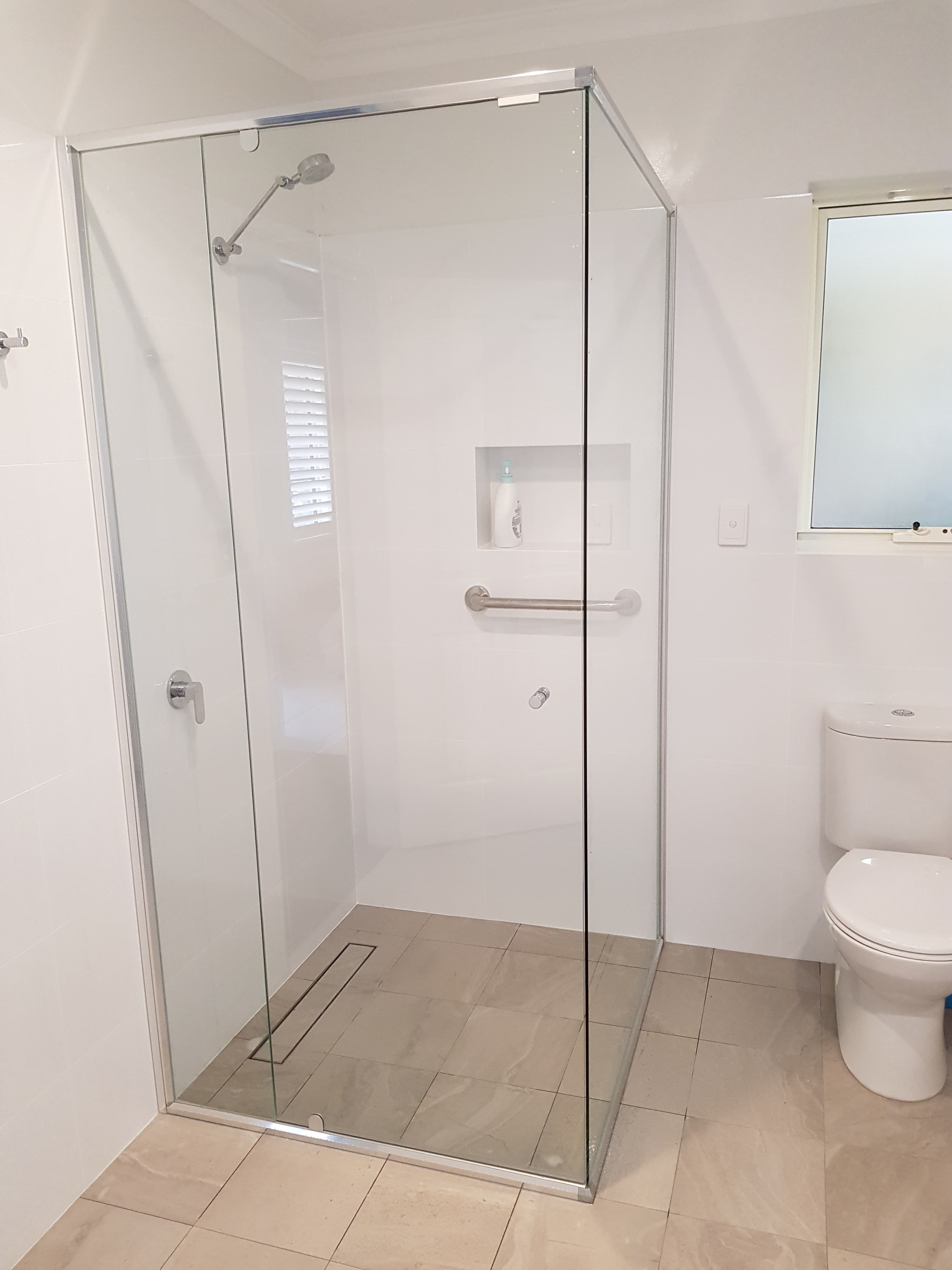 Modern white tiled bathroom with a glass shower stall, chrome fixtures, and a white toilet.