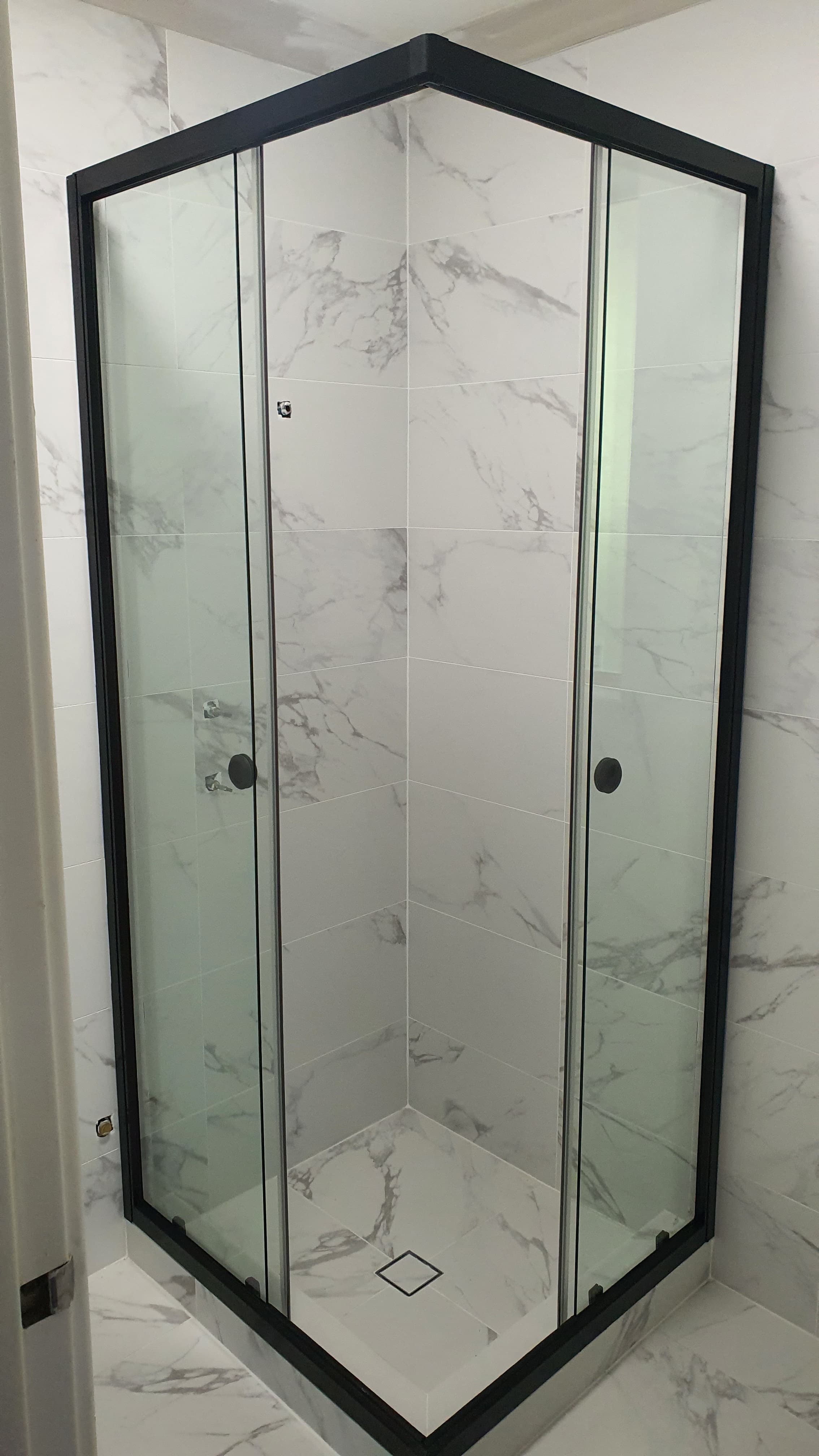 Modern corner glass shower with black frames and white marble-patterned tile walls and floor.