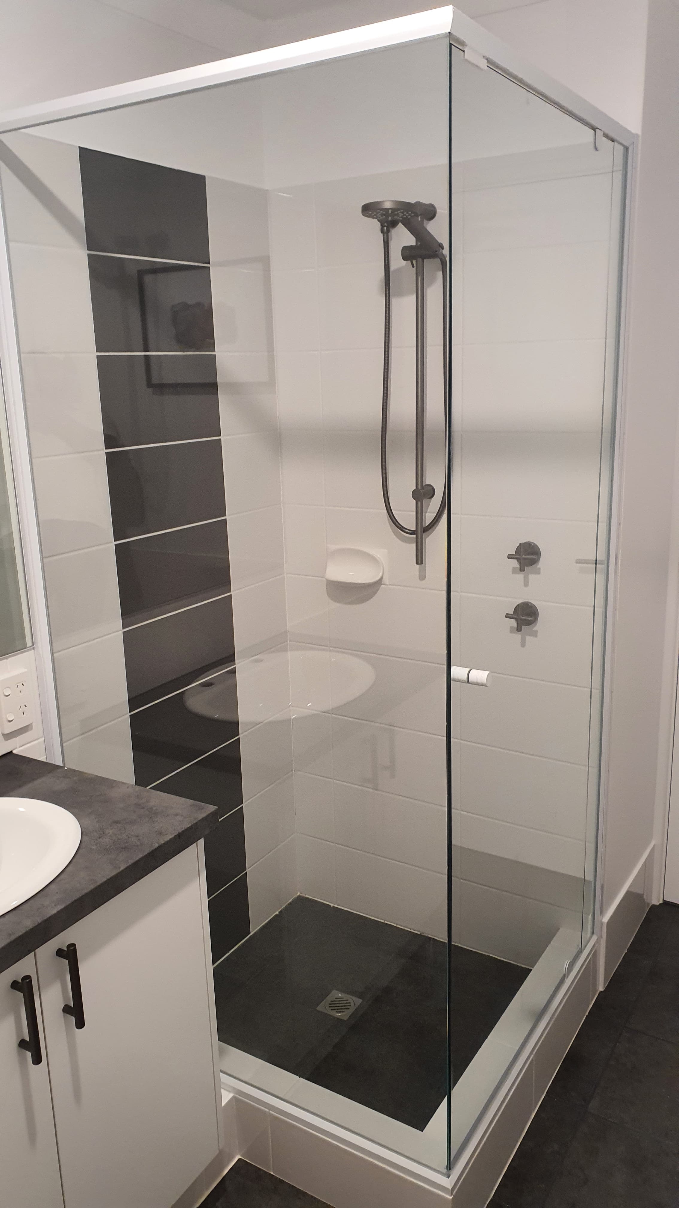 Glass-enclosed shower with white wall tiles, a dark grey accent stripe, and black metal fixtures.