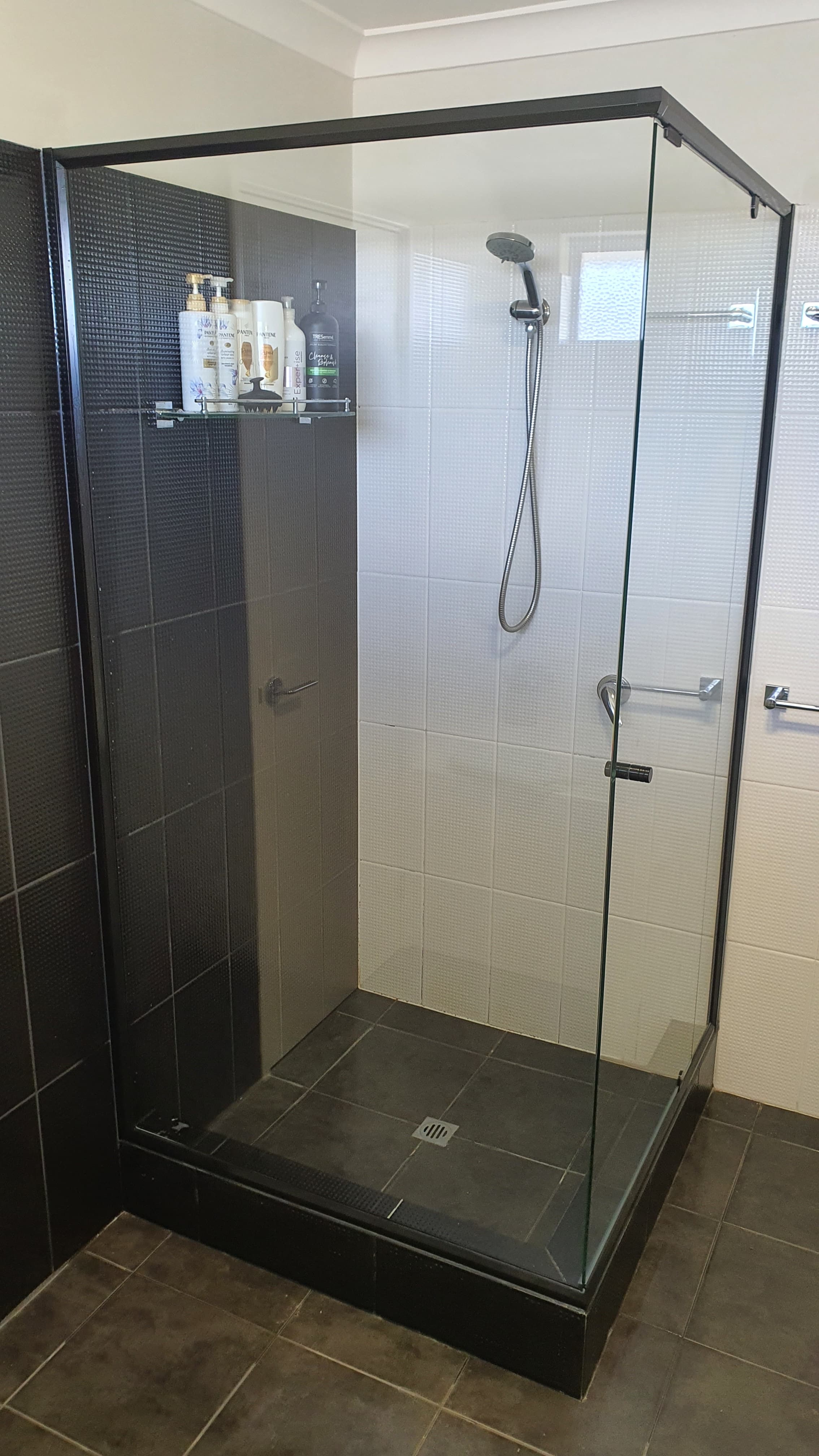 Modern glass shower enclosure featuring contrasting black and white tiles with chrome fixtures and toiletries.
