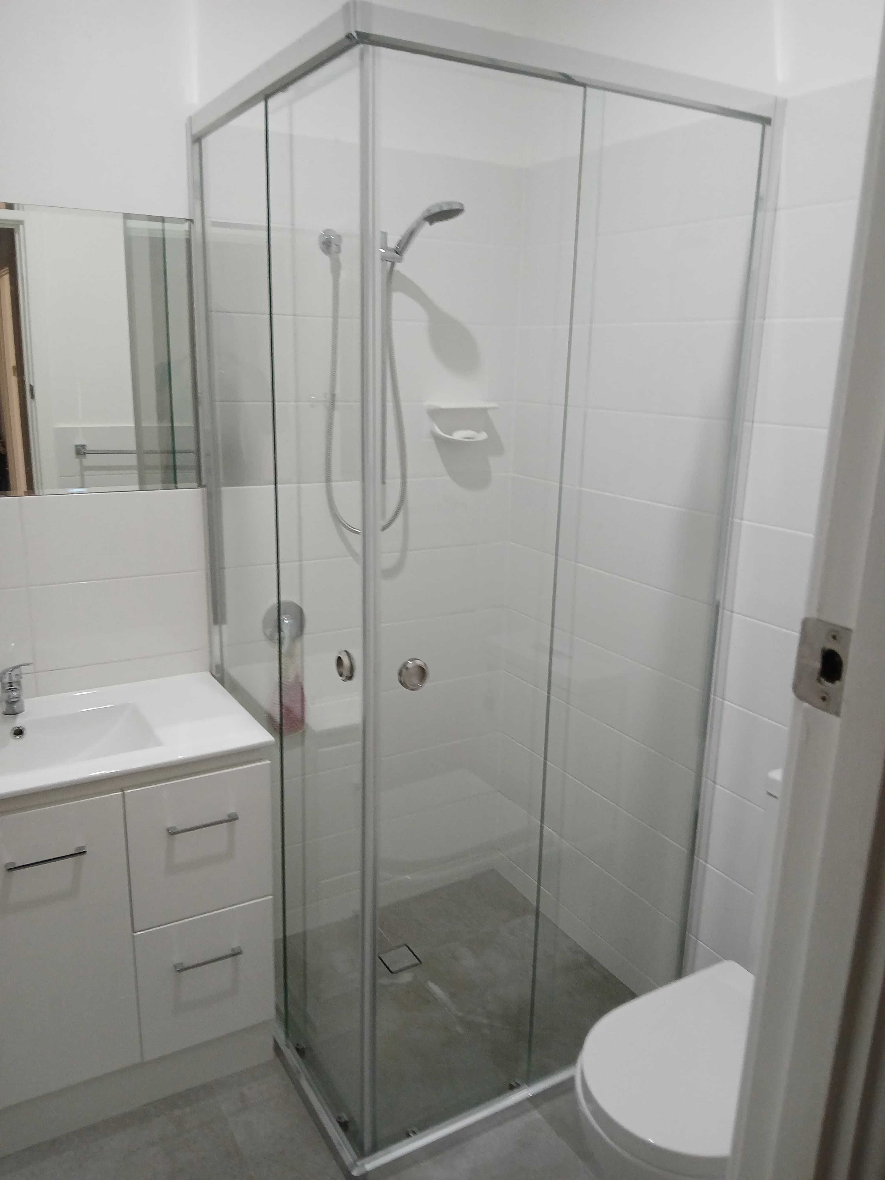 Modern white bathroom with a glass corner shower, white vanity, and white tiled walls.