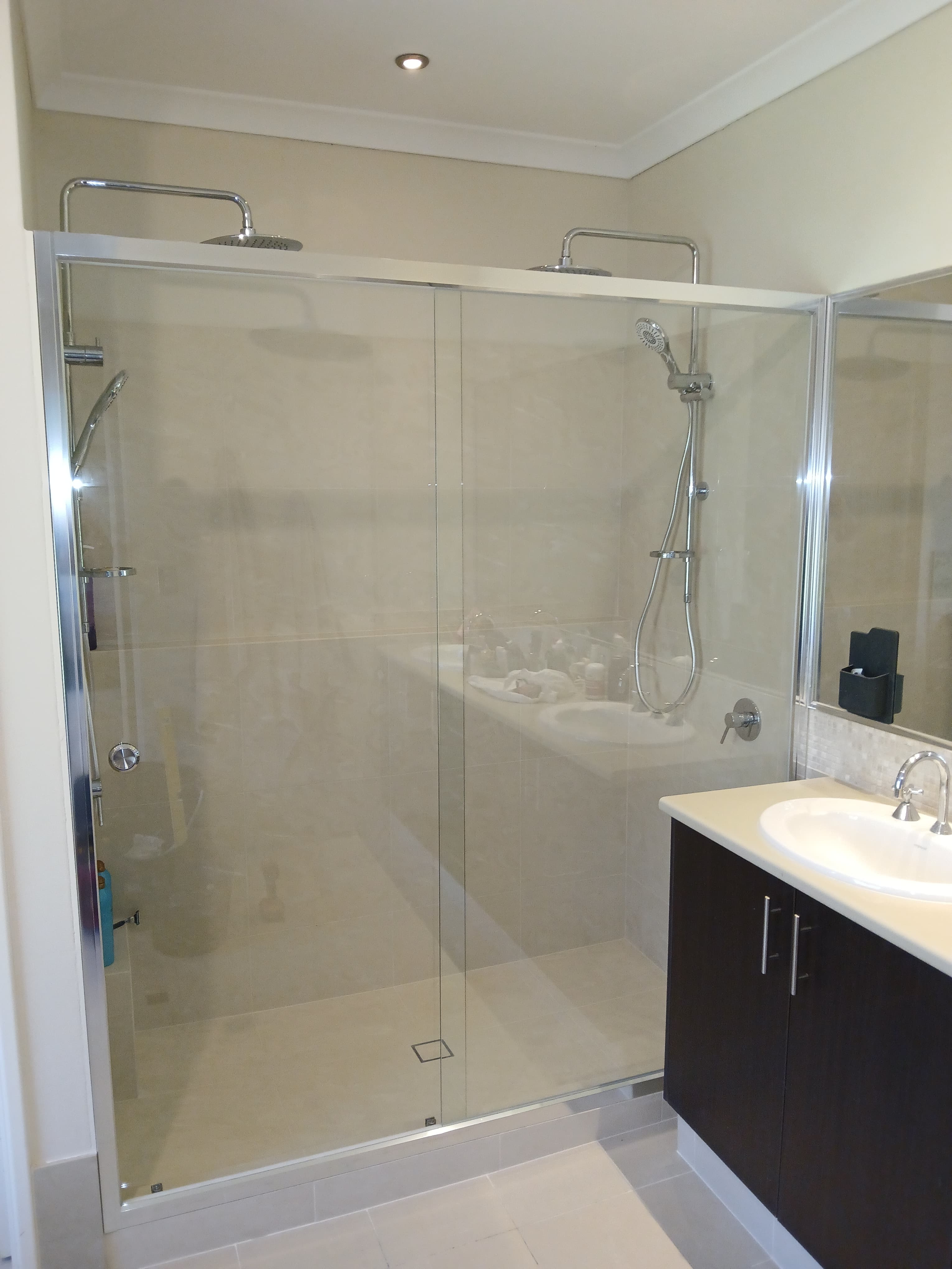 Modern bathroom featuring a large glass shower with dual rainfall heads and dark wood vanity.