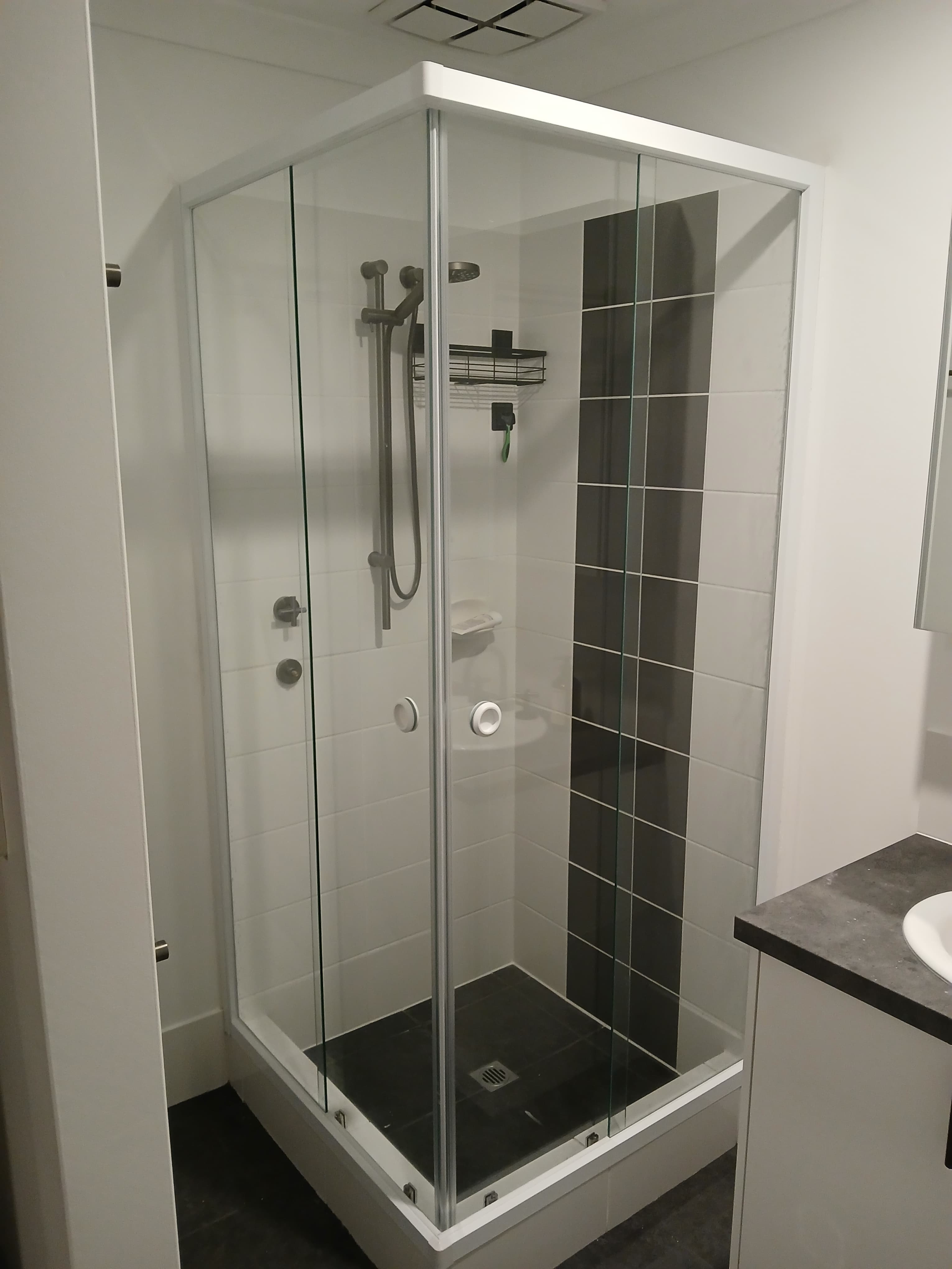 Modern glass corner shower with white tiled walls and a vertical black tile accent.