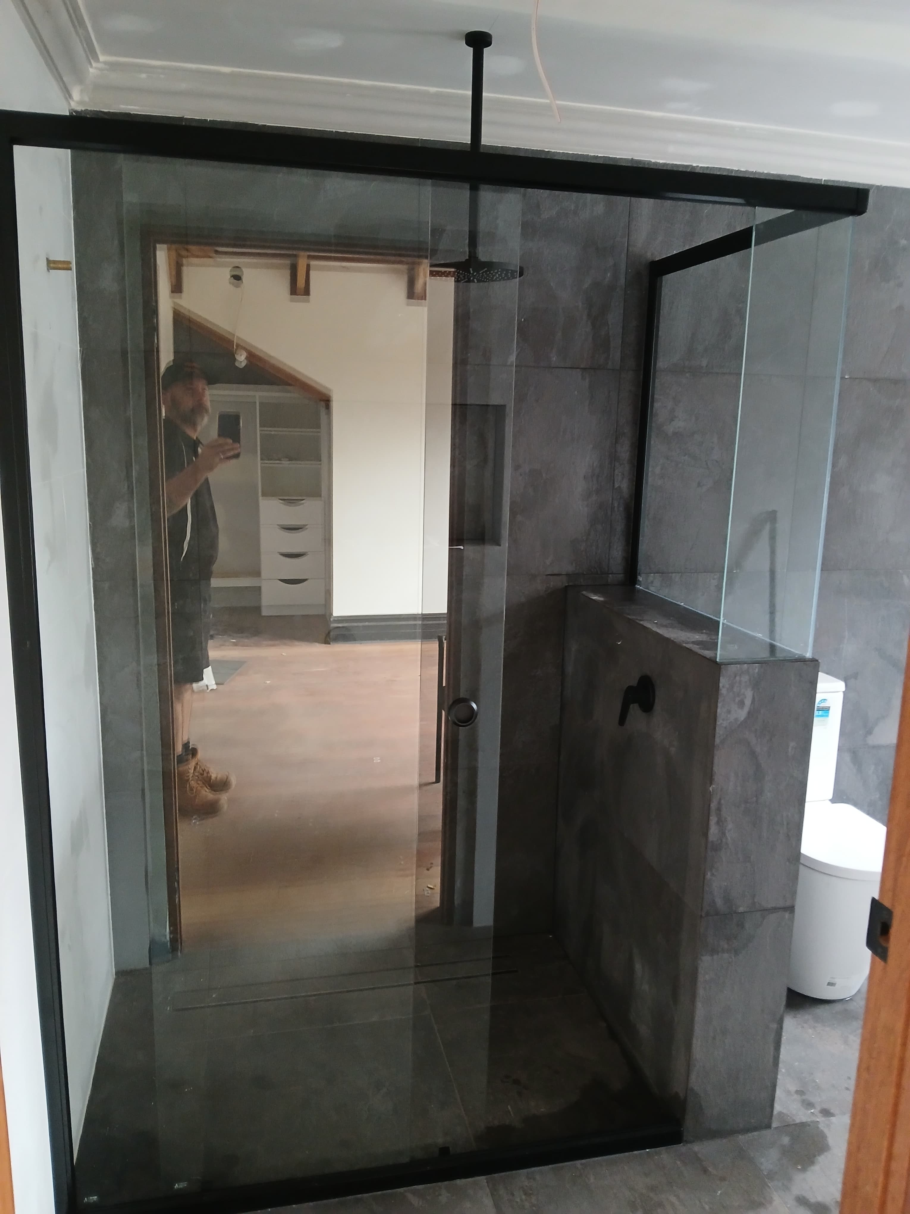 Modern walk-in shower with black-framed glass, dark gray tiles, and a ceiling-mounted rain showerhead.