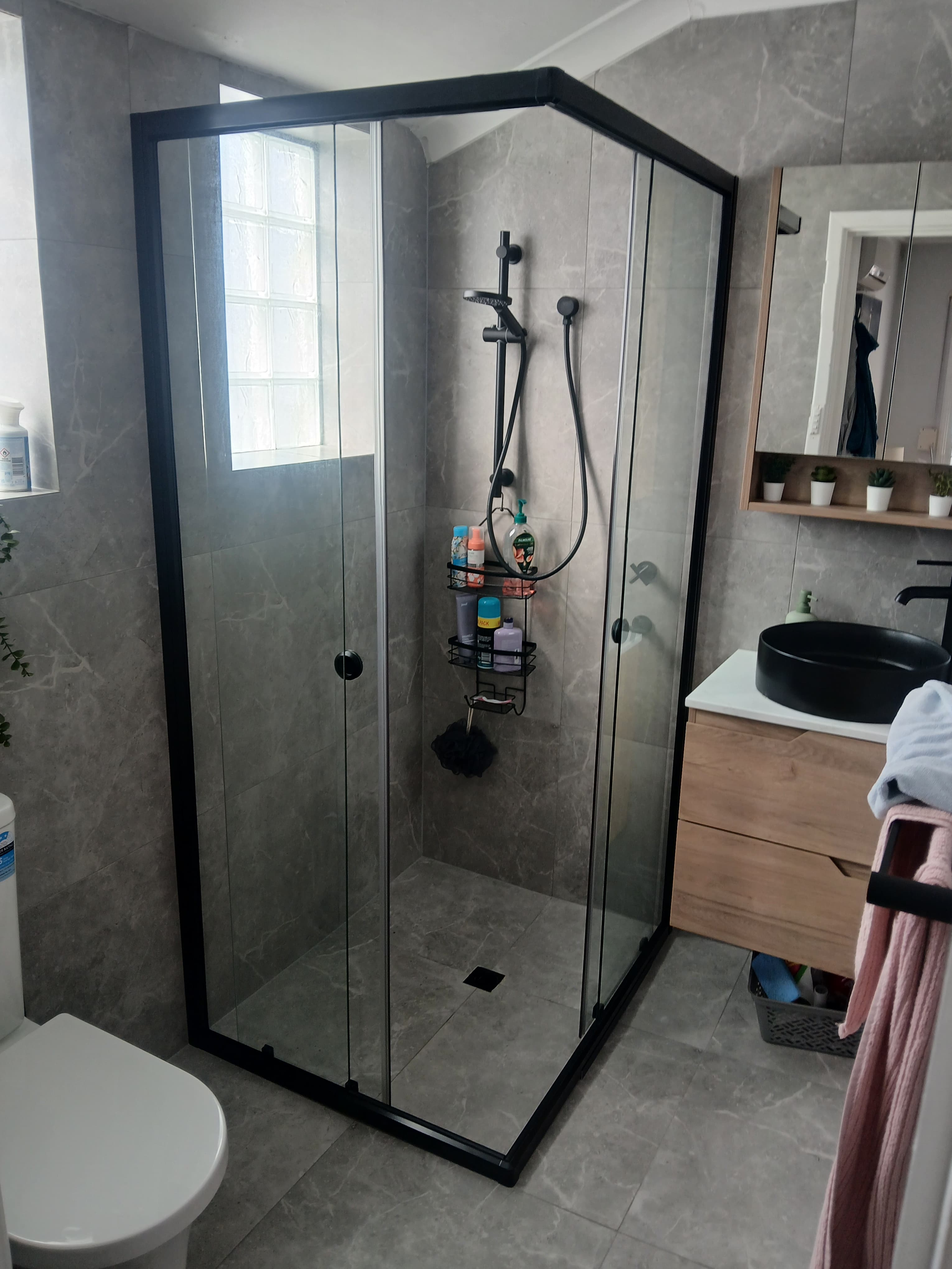 Modern bathroom featuring grey marble tiles, a black-framed glass shower, and a wooden vanity.