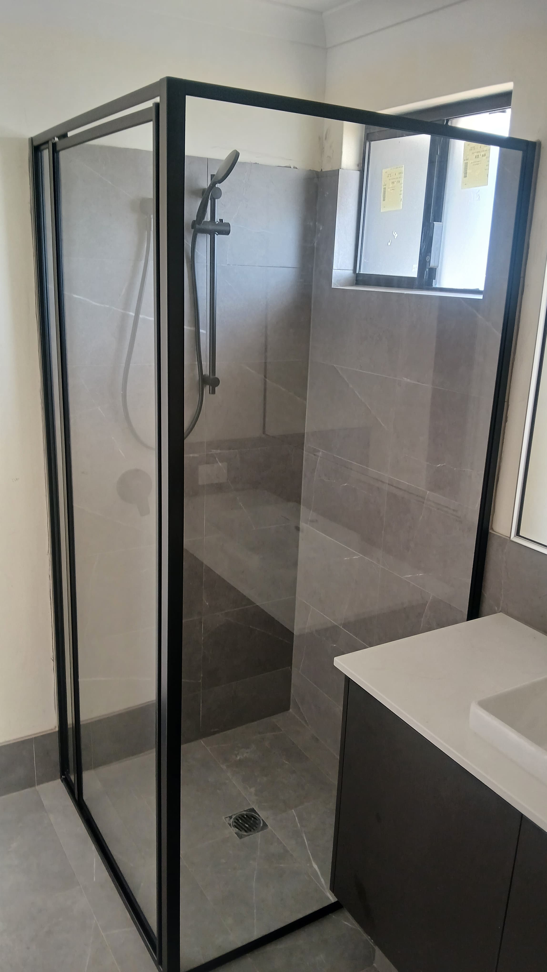 Modern glass shower with black frame, grey marble tiles, and a white bathroom vanity.