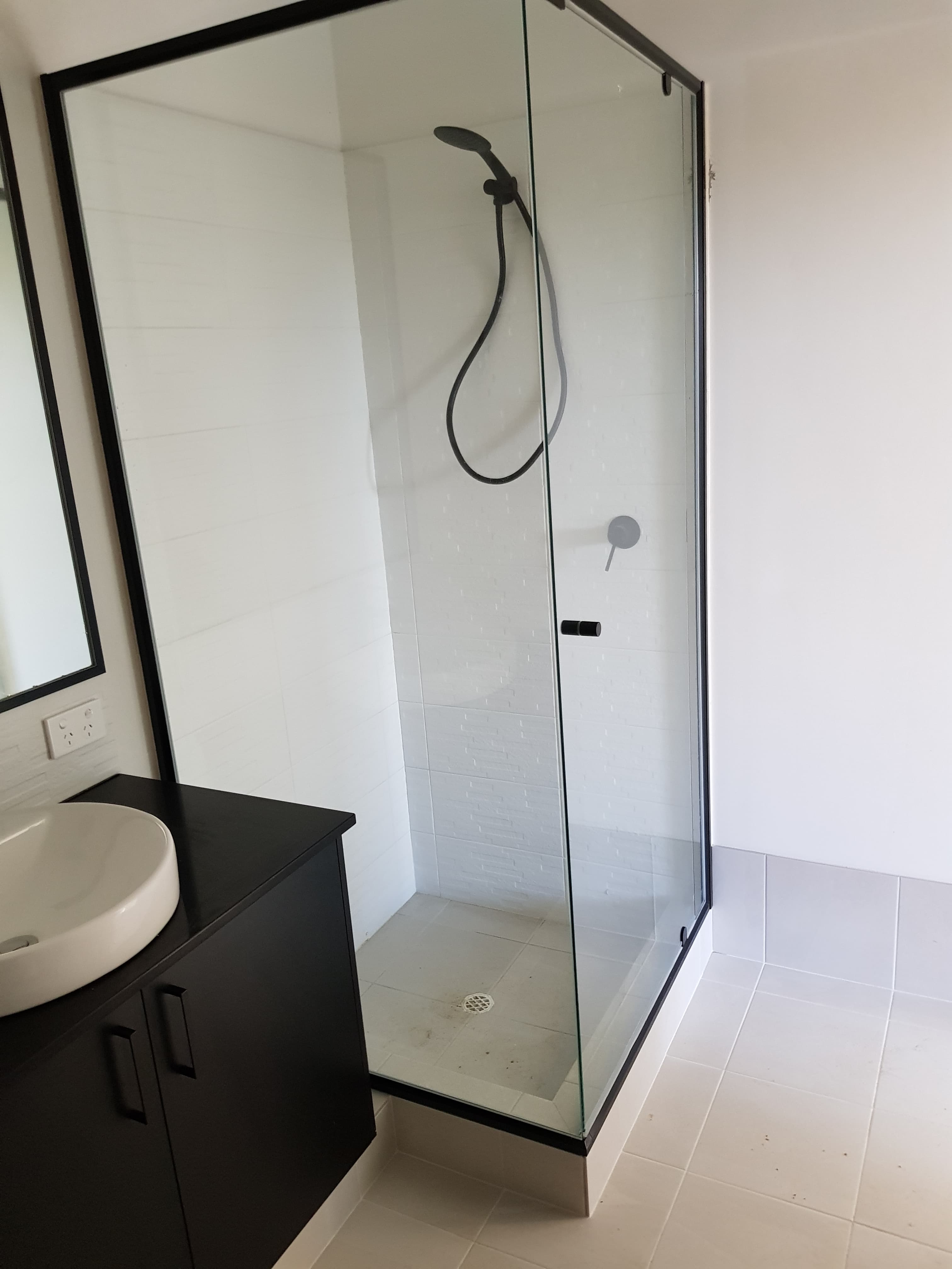 Modern bathroom featuring a black-framed glass shower and a black vanity with white vessel sink.