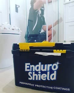 Technician applying EnduroShield protective coating to a glass shower screen behind a branded black toolbox.