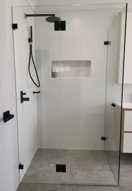 Modern walk-in shower featuring frameless glass, matte black fixtures, and grey stone floor tiles.