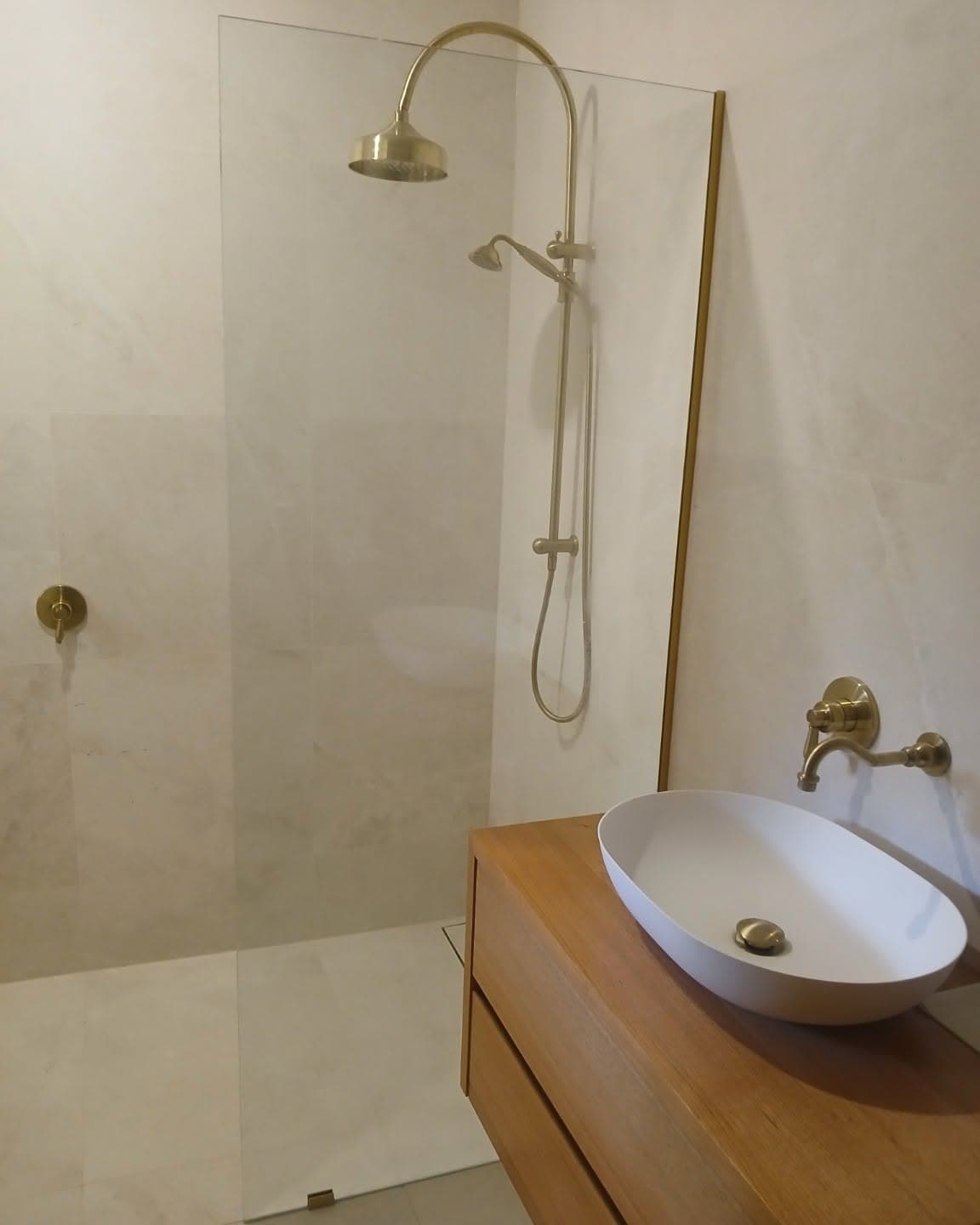 Modern bathroom featuring gold shower fixtures, glass partition, and wooden vanity with white vessel sink.