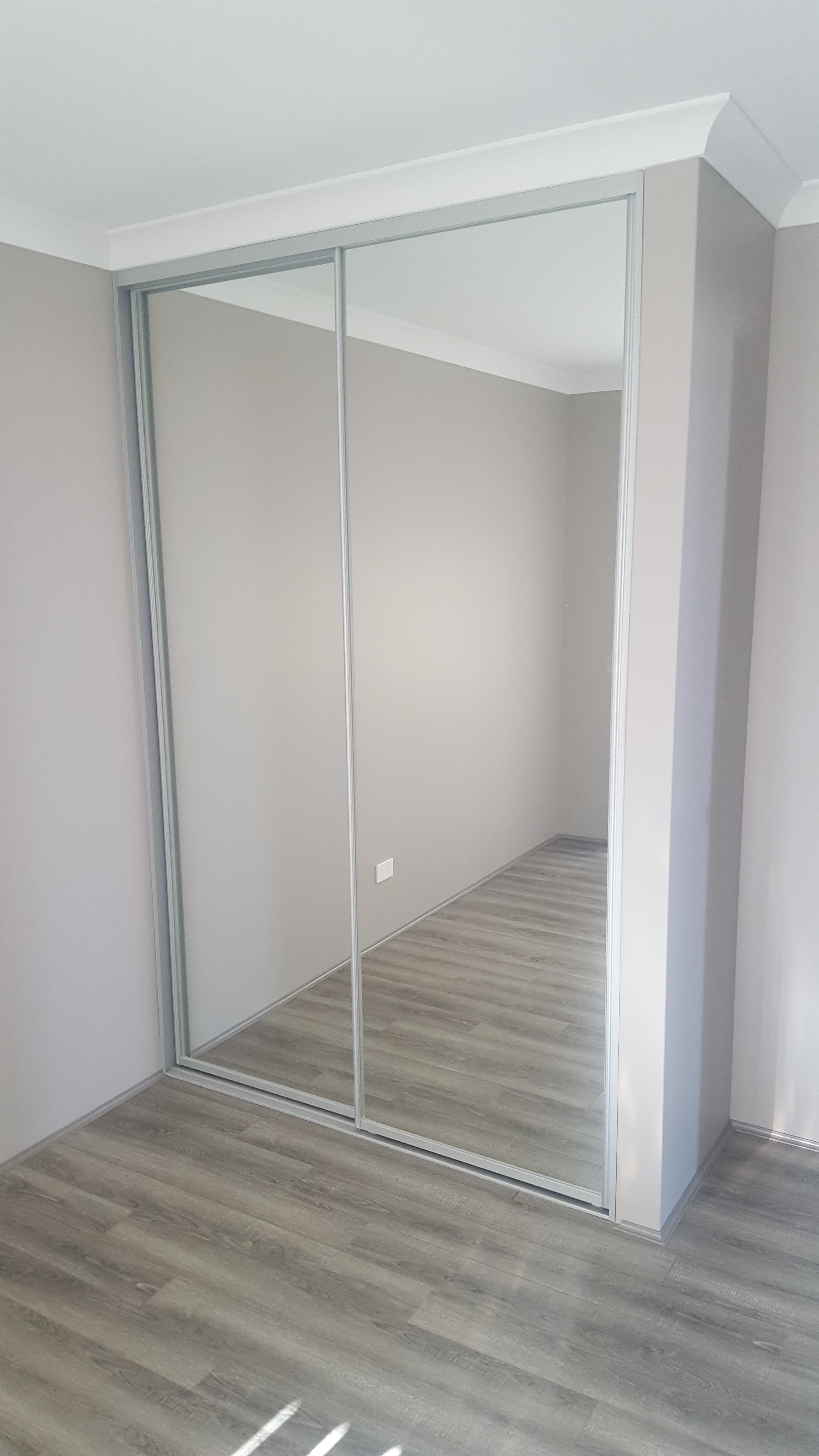 Modern built-in wardrobe featuring two large sliding mirrored doors and a slim silver frame.